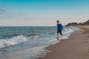 A little boy runs along the coast of the sea, the ocean. Leisure activities in the summer.