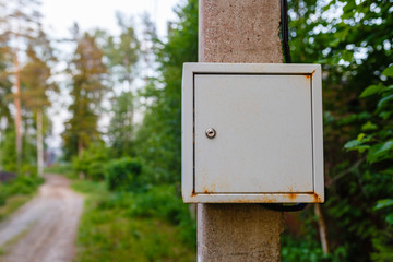 Old electric shield on a concrete pole in the countryside near a dirt road. The old electric shield, a rusty metal box hangs on the pole electric pole of the garden