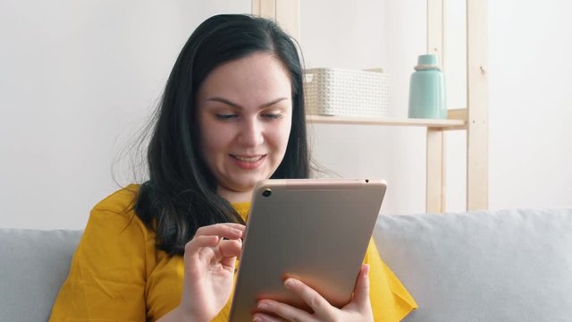 Portrait of a young beautiful woman in yellow t-shirt who uses a tablet.