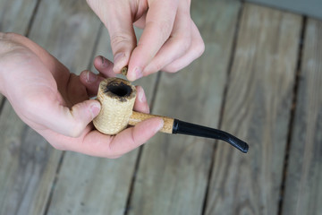 Caucasian male packing a corn cobb pipe with marijuana.