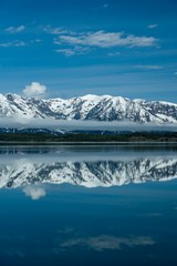 Snow covered mountains reflecting in calm lake with beautiful blue sky and clouds