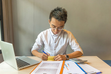 Fototapeta premium Asian businessman reading financial report and writing notes