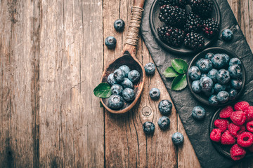 Fresh berries with raspberries, blueberries, blackberries in bowl on a stone stand on wood background.