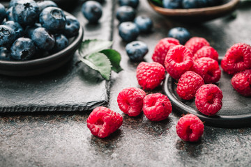 Fresh berries with raspberries, blueberries, blackberries in bowl on a stone stand on a dark metal background.