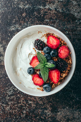 Healthy breakfast with granola, yogurt, fruits, berries on dark metal background. Summer homemade breakfast.