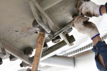 Workers use a wrench to loosen the nut by using a large hammer.  To open the metal manhole. The manhole is position overhead.