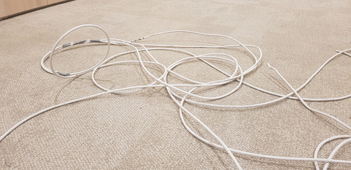 White electric cables on the brown carpet floor. Cluttered and tangled