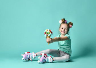 Kid girl in roller skates sits on the floor at free text copy space holds a big and tasty ice-cream in waffles cone