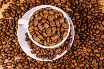 White cup filled with coffee beans on wooden table. Top view