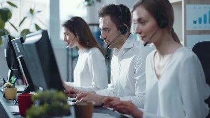 Slow motion colleagues young people operator taking calls smile in call center office business worker computer corporate headset job man service group finance sunshine phone close up - Powered by Adobe