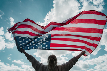 Closeup back view of a Proud woman enjoying summer sunset outdoors and holding american flag.