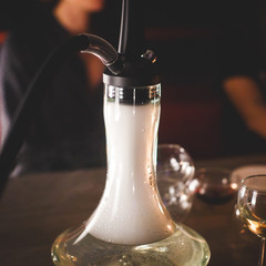 View of Hookah with candles and smoke on a table, hookah lounge with young people smoking in the background, shisha party club concept