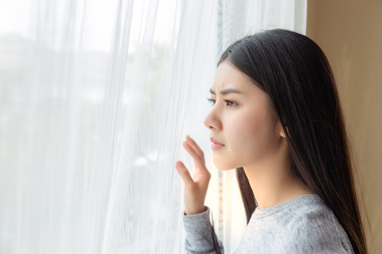 Charming beautiful young woman look through window and looking something that make her getting suspicious. Attractive beautiful girl look stressed and nervous because asian woman stay alone at home