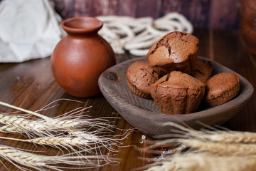 chocolate cupcakes in a wooden plate on the background of a clay jug