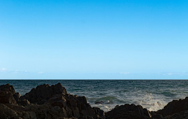 Fototapeta na wymiar Seascape. Blue clear sky and black rock. Calm sea