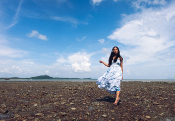 Asian girl wear Indigo dyed cotton long skirt,smiling and flower tucked behind her ear on the beach,blue sky and sea,orange light flare.