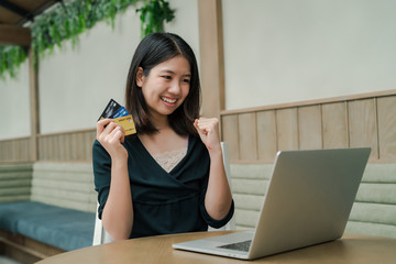 Closeup Asian beautiful woman Wearing a black shirt Sitting in the house Have a credit card in hand Is buying online products with a laptop computer