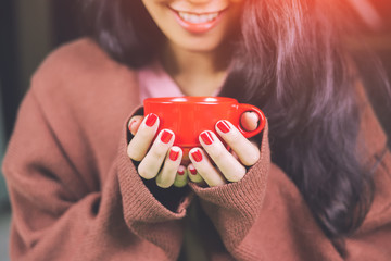 Asian women holding a red cup of coffee.