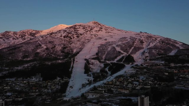Aerial view of mountain in sunset with ski slope close to a city. MOVING FORWARD.