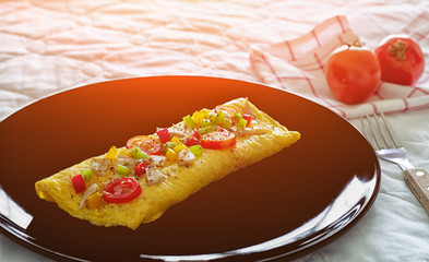 Omelette, egg roll with a topping in a black plate on cement, there are sliced tomatoes, shoped bell peppers and mushrooms.colorful decorate food for kid