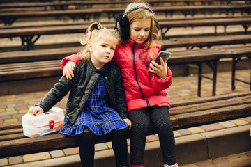 Two cute kids in a park. Children playing. Girls sitting with phones