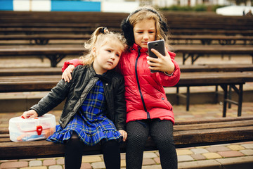 Two cute kids in a park. Children playing. Girls sitting with phones