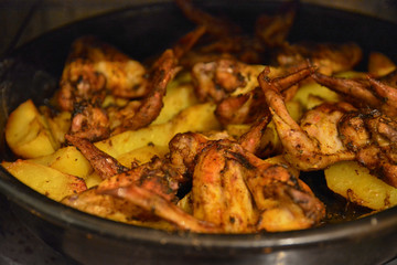 Baked fried potatoes with delicious fried chicken wings with golden crust served with sauces in black bowl on wooden table background. Selective focus.