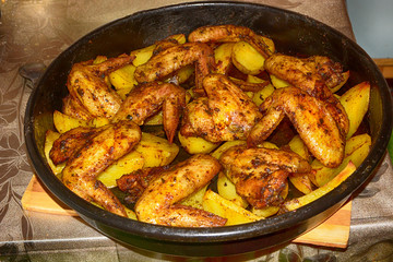 Baked fried potatoes with delicious fried chicken wings with golden crust served with sauces in black bowl on wooden table background. Selective focus.