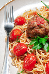 Pasta with meatballs and tomato sauce. Decorated with greens and roasted cherry tomatoes. In the original plate. On the plate lies a fork. View from above. Macro. Large background. 