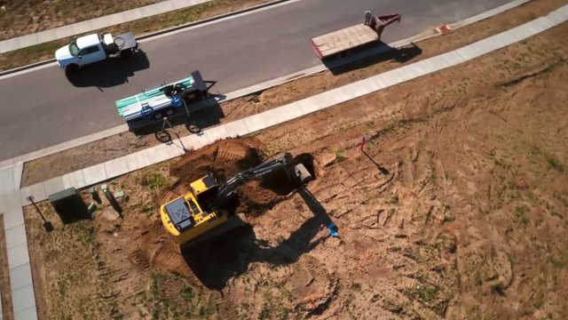 A drone shot spinning around some construction machinery digging a fresh hole in the ground where a new house will soon be one day.