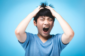 Portrait of angry asian kid on blue background.