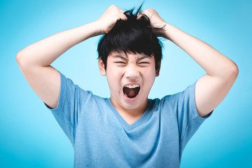 Portrait of angry asian kid on blue background.