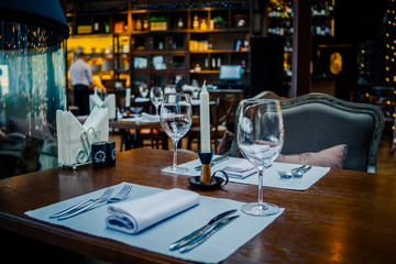 Glasses, flowers, fork, knife served for dinner in restaurant with cozy interior, retro film filter effect.Selective focus.Restaurant interior, modern setting, wine glasses,on textile napkins. Concept