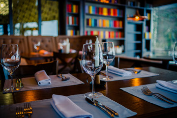 Glasses, flowers, fork, knife served for dinner in restaurant with cozy interior, retro film filter effect.Selective focus.Restaurant interior, modern setting, wine glasses,on textile napkins. Concept