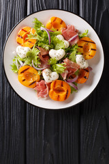 Easy dietary salad with mozzarella, prosciutto, grilled apricots, red onion and lettuce close-up on a plate. Vertical top view