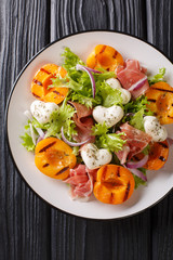 Delicious romantic salad with mozzarella, ham, apricot grilled and fresh lettuce close-up on a plate. Vertical top view