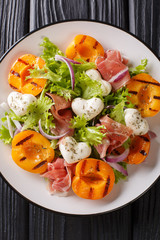 Italian salad with mozzarella, prosciutto, grilled apricots, red onion and  lettuce close-up on a plate. Vertical top view