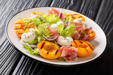 Italian summer salad with mozzarella cheese, prosciutto, grilled apricots, red onion and leaf lettuce close-up. horizontal