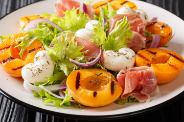 Italian salad with mozzarella, prosciutto, grilled apricots, red onion and  lettuce close-up on a plate. horizontal