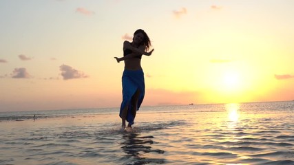 Young beauty girl dancing at tropical beach on sea water at paradise island at sunset . Summer concept. Holiday travel, slow motion