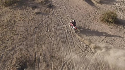 AERIAL: Overhead dynamic shot of a dirt biker as he does a few quick skidding turns on his Honda CRF motorcycle in the desert and takes off into the distance. - Powered by Adobe
