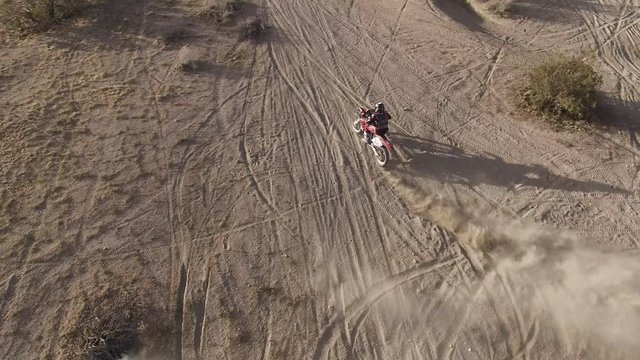 AERIAL: Overhead dynamic shot of a dirt biker as he does a few quick skidding turns on his Honda CRF motorcycle in the desert and takes off into the distance.