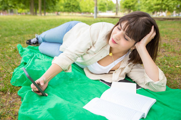 Happy relaxed student girl consulting internet in park. Young woman lying on grass outdoors and using smartphone. Internet connection outdoors concept