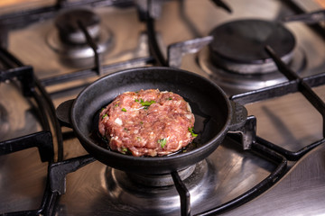 Iron pan with raw cutlet on a gas stove.