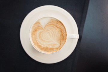 Cup of coffee on black table background with beautiful latte art heart shaped.