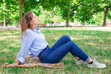 Relaxed young woman enjoying fresh air in park. Peaceful girl with wavy hair keeping eyes closed while resting alone. Serene woman concept