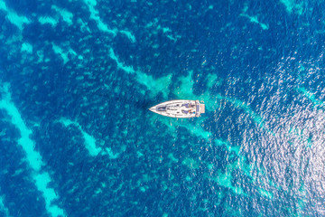 Pleasure white yacht with sail stands on coral reef in blue transparent turquoise water. Concept travel. Aerial top view.