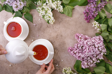 Tea set and flower decor on a textural background. Pouring tea into a mug and place under the text. View from above. Flat lay. The concept of tea drinking.