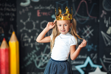 Cute little girl with princess crown drawing above head studying at classroom.