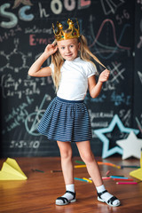 cute little schoolgirl against chalkboard with school formulas, with a gold crown on her head